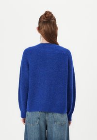 Blue knitted sweater with long sleeves and a round neckline, featuring a textured fabric and a relaxed fit. Worn with high-waisted jeans.