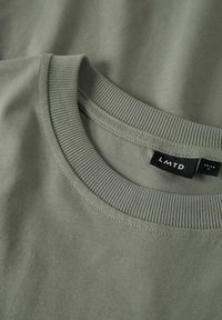 Maslinasto zeleni T-shirt s rebrastim okruglim izrezom. Mekana pamučna tkanina s glatkom teksturom. Na etiketi je prikazan brend LM TD i veličina 13-14.