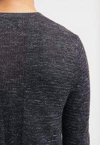 Pull en maille gris foncé avec une surface texturée. Présente un col rond et des variations de couleur subtiles, mettant en valeur un tissu doux.
