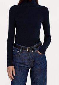 Pull à col roulé côtelé marine associé à un jean en denim noir et une ceinture en cuir noir avec une boucle dorée. Design simple et ajusté.