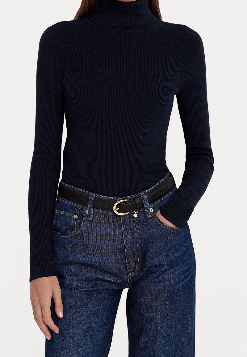 Pull à col roulé côtelé marine associé à un jean en denim noir et une ceinture en cuir noir avec une boucle dorée. Design simple et ajusté.