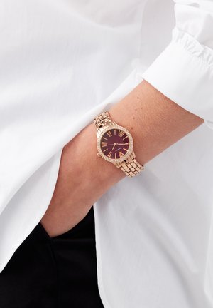 Montre-bracelet en or rose avec un cadran rond bordeaux, des chiffres romains et des accents étincelants. Le bracelet présente un design à maillons.