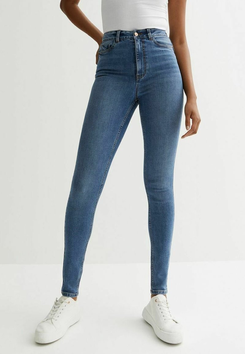 Skinny blue denim jeans with a high waist and a classic five-pocket design. Paired with white sneakers on a neutral background.
