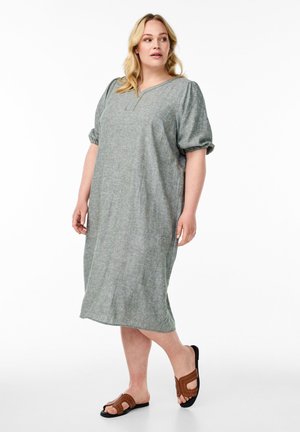 Grön texturerad klänning med v-ringning och puffärmar, stiliserad till knälängd. Matchad med bruna sandaletter med utskärningar och nitar.