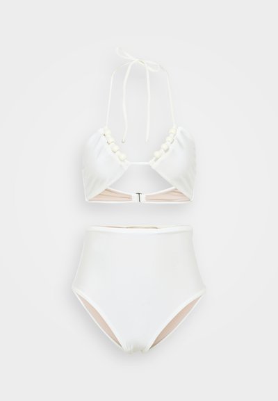 Bela kopalna oprema s halter vratnim vrhom, ki vključuje biserne detajle in zaponko, v kompletu z visokim pasom kopalk. Gladka tekstura.