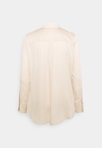 Beige long-sleeve shirt with a subtle dot pattern, collar, and buttoned cuffs. Back features a yoke and a central pleat for ease of movement.