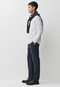 Chemise à manches longues rayée blanc et bleu marine, écharpe gris foncé drapée, pantalon bleu marine et chaussures à lacets noires. Textures lisses, coupe classique.