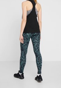 Svart atletisk linne med racerback-design, kombinerat med åtsittande turkosa leggings med svart zebramönster, bärs tillsammans med svarta sneakers.