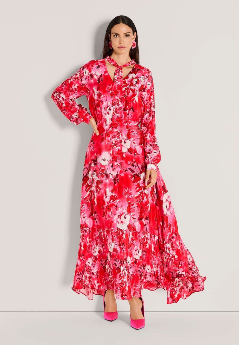 Langes Blumenkleid in verschiedenen Rosatönen, mit langen Ärmeln, einer Schleife am Hals und einem fließenden Saum. Glatter Stoff mit einem lebhaften Blumenmuster.