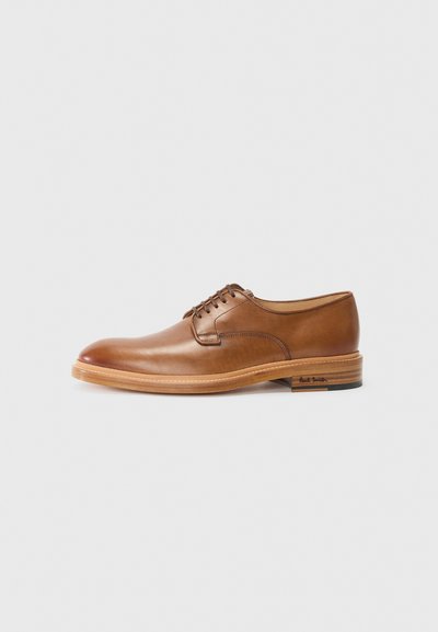 Zapato de cuero marrón con cordones, punta redondeada, suela clara en contraste y un sutil logo en el talón. Textura suave y diseño clásico.