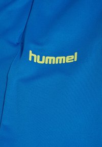 Blauwe sportkledingstof met een gem textureerd oppervlak en een opvallend geel "hummel" logo aan één kant. Eenvoudig ontwerp en atletische stijl.