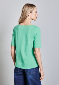 Krátký rukáv, top ze světle zelené bavlny s lodními výstřihem a volným střihem, doplněný tmavě modrými denimovými kalhotami. Hladká textura, ležérní design.