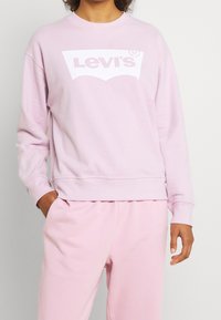 Sweat-shirt rose avec un logo Levi's blanc. Encolure ronde, manches longues, coupe décontractée et poignets côtelés. Tissu doux en mélange de coton.