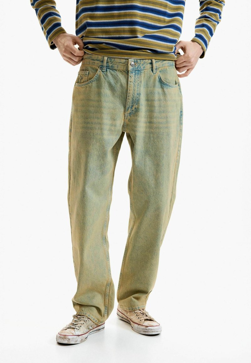 Faded light blue denim jeans with a relaxed fit, featuring a classic five-pocket design and subtle vertical texture. Worn with beige sneakers.