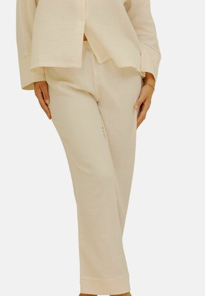 Pantalons en tissu texturé beige clair, avec une coupe décontractée, présentant une jambe droite et sans fermetures visibles, complétant un haut assorti.