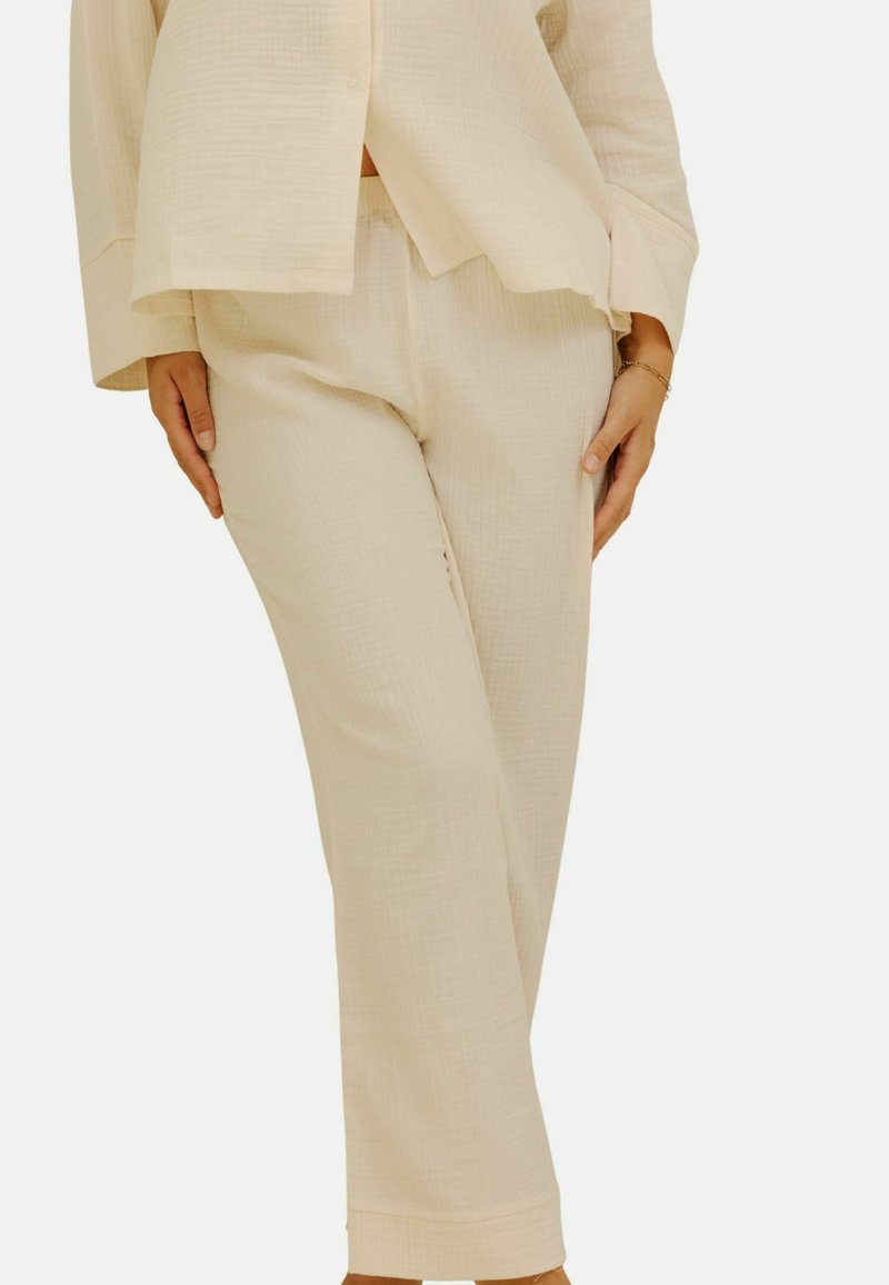 Pantalons en tissu texturé beige clair, avec une coupe décontractée, présentant une jambe droite et sans fermetures visibles, complétant un haut assorti.