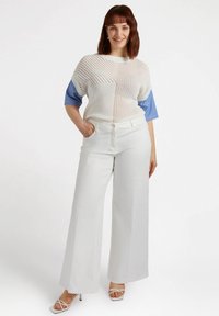 Biała sweter z dzianiny z krótkimi rękawami w niebieskie paski, zestawiony z szerokimi białymi spodniami i białymi sandałami na obcasie. Płaskie kieszenie z przodu i z boku.
