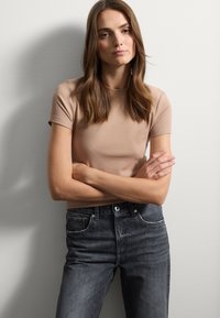 Camiseta de punto ajustada beige de manga corta combinada con unos vaqueros de talle alto gris oscuro que cuentan con bolsillos frontales y cierre de botones.