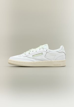 Weißer niedriger Reebok-Sneaker mit elfenbeinfarbener Sohle, perforierter Zehenpartie und genähten Lederpaneelen, seitlich auf neutralem Hintergrund gezeigt.
