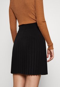Gonna plissettata nera con vita alta, caratterizzata da una texture liscia e una silhouette fluida, abbinata a un top a manica lunga marrone a coste.