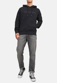 Hættetrøje i sort bomuld med en frontlomme, prydet med et hvidt logo. Parret med grå denimjeans og sorte sneakers.