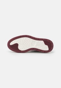 Semelle de chaussure avec des motifs en caoutchouc bordeaux et blanc, présentant des rainures et des crêtes courbes pour la traction et l'adhérence.