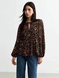 Blouse en imprimé léopard marron et noir avec un col �à ouverture en forme de clé et un détail froncé, associée à un jean en denim bleu. Manches longues avec poignets élastiques.