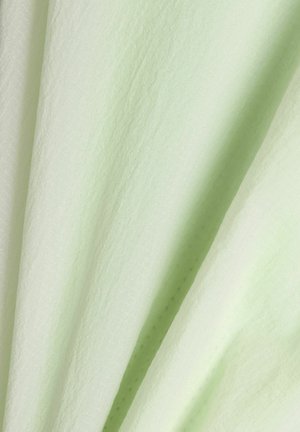 Lichtgroene gestructureerde stof met subtiele patronen en zachte plooien die zachte schaduwen en diepte creëren.