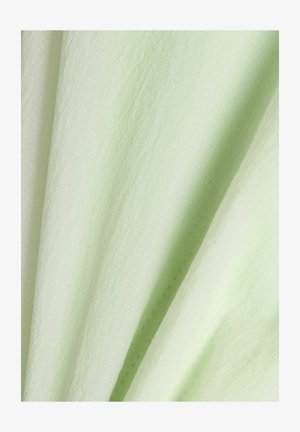 Tissu vert clair texturé avec des motifs subtils et de doux plis créant des ombres douces et de la profondeur.