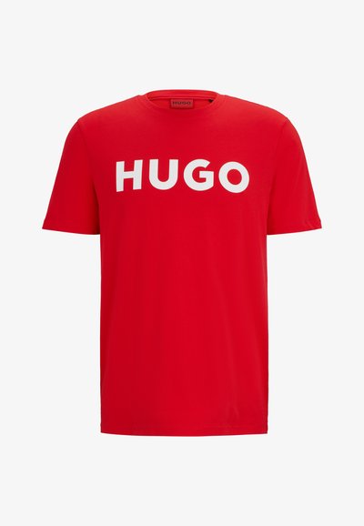 T-shirt en coton rouge avec un logo "HUGO" blanc audacieux sur la poitrine. Manches courtes et col rond standard. Texture douce.