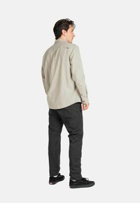 Light gray long-sleeve shirt with a curved hem and button cuffs, paired with dark pants and black shoes, viewed from the back.