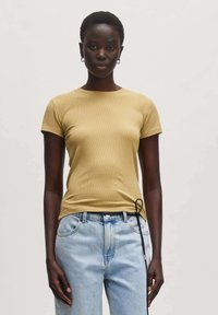Getailleerd geribbelde t-shirt in lichtgeel met korte mouwen en ronde hals. Gecombineerd met lichtblauwe jeans met een trekkoordaccent.