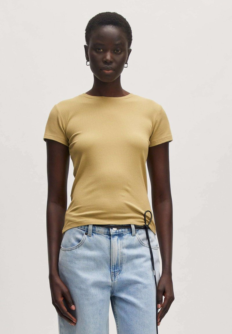 Getailleerd geribbelde t-shirt in lichtgeel met korte mouwen en ronde hals. Gecombineerd met lichtblauwe jeans met een trekkoordaccent.
