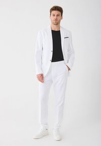 Biały garnitur o dopasowanym kroju, z marynarką zapinaną na jeden guzik i dopasowanymi spodniami. Czarna koszulka z okrągłym dekoltem pod spodem. Białe trampki.