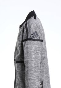 Giacca sportiva grigia con tessuto texturizzato, dettagli neri sulle spalle, tasche con zip e logo Adidas sulla parte superiore del braccio.