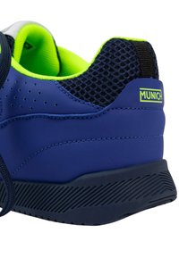 Zapatilla deportiva azul marino con acentos de malla, forro verde neón, detalles perforados y una suela de goma negra texturizada. Logo "MUNICH" visible.