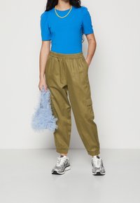 Blå kortärmad topp, olivgröna cargobyxor med elastisk midja, ljusblå fluffig tote-väska och silverfärgade sneakers med svarta accenter.