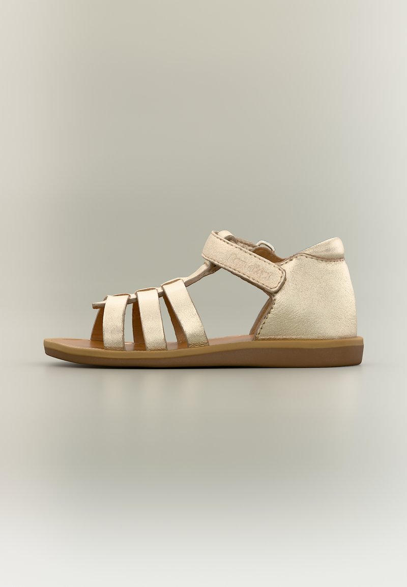 Παιδικό μεταλλικό χρυσό σανδάλι με τρεις μπροστινές λουρίδες, λουρίδα στον αστράγαλο με αυτοκόλλητο κλείσιμο και επίπεδη καφέ σόλα σε ουδέτερο φόντο.