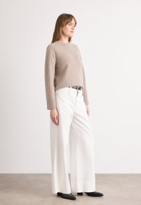 Beige vlněný svetr s kulatým výstřihem, doplněný o široké bílé kalhoty. Černý opasek a špičaté černé boty dotvářejí celý outfit.