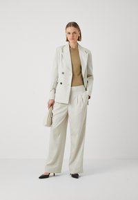 Svetlý dvouřadý blazer s černými knoflíky v kombinaci s ladícími skládacími kalhotami. Hnědý přiléhavý top a černé špičaté podpatky.