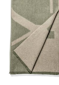 Tapis rectangulaire avec une texture douce, featuring un fond vert kaki et un motif géométrique beige contrastant. Les bords sont effilochés, ajoutant du détail.