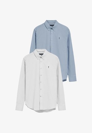 To skjorte med knaplukning: en lyseblå og en hvid. Begge har en klassisk krave, lange ærmer og et lille logo på brystet.