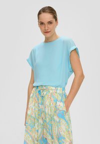 Blouse à manches courtes bleu clair avec un col rond, associée à une jupe maxi multicolore à motifs avec une taille à cordon.