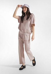 Felpa rosa oversize e pantaloni abbinati a taglio ampio realizzati in tessuto morbido, completati da un cappello bianco e scarpe nere stringate.