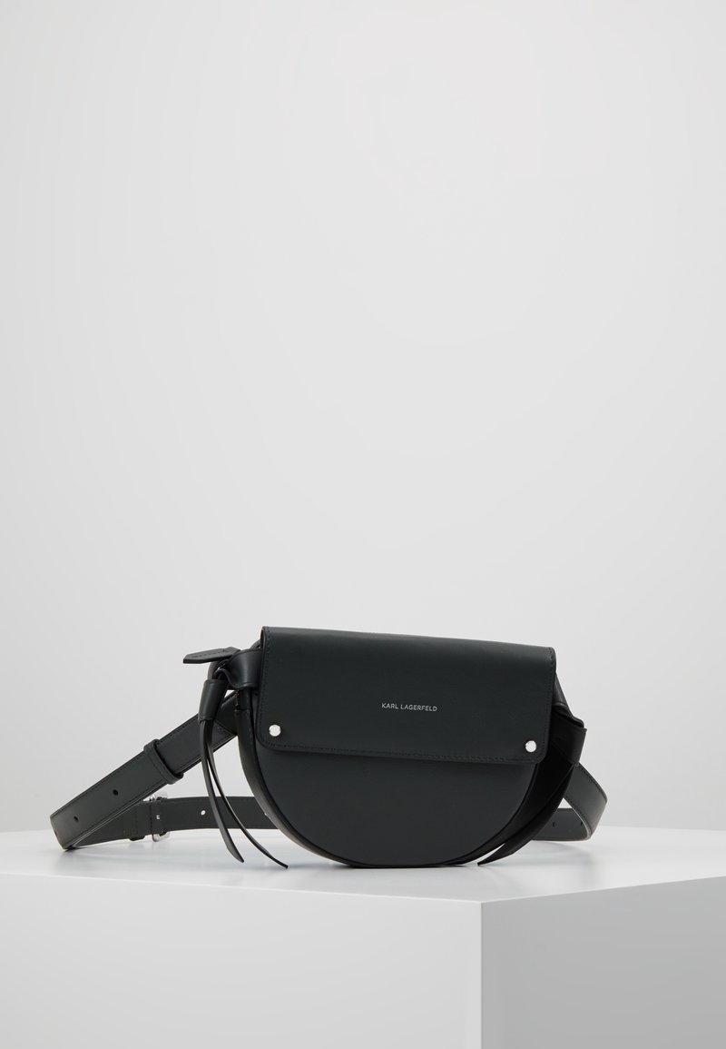 Zwarte leren crossbodytas met een afgerond ontwerp, voorzien van een klep sluiting, zilverkleurige hardware accenten en een verstelbare riem.