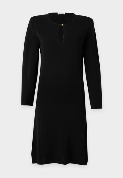 Robe noire longue à manches longues, longueur genou, avec un col rond et une petite ouverture en forme de serrure fermée par un seul bouton doré au niveau de la poitrine.