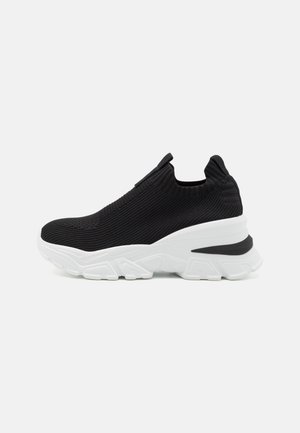 Fekete kötött slip-on sportcipő fehér, vastag talppal, texturált anyaggal és hátsó húzófüllel a könnyű felhúzás érdekében.