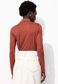 Haut à manches longues de couleur rouille en tissu doux, associé à une jupe en jean blanche taille haute, longueur genou, avec des coutures visibles et des poches.