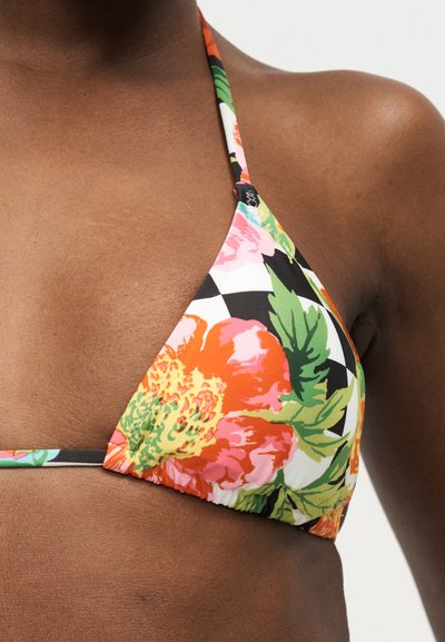 Κοντινό πλάνο ενός ατόμου που φοράει πολύχρωμο μπικίνι με λουλούδια, πράσινα φύλλα και πορτοκαλί, ροζ και κίτρινα λουλούδια σε μαύρο-άσπρο φόντο με σχέδιο.