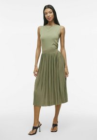 Abito midi plissettato verde oliva con corpetto aderente e design senza maniche. Abbinato a tacchi aperti neri. Texture del tessuto liscia.